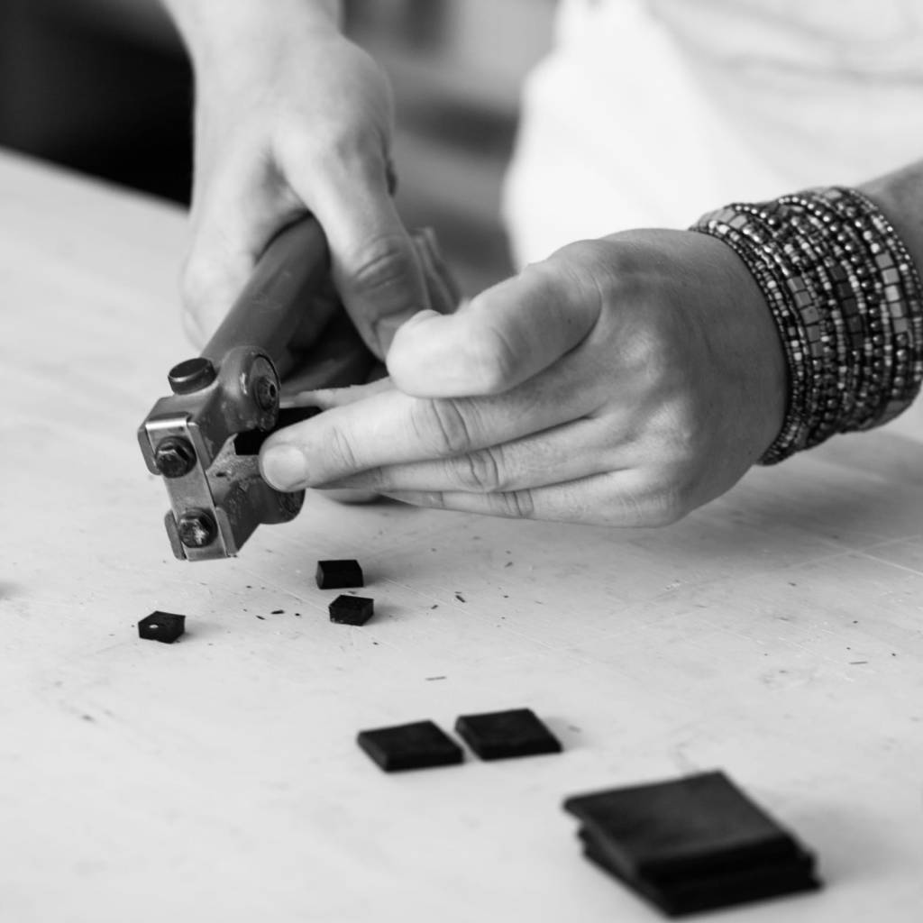 Une main tenant un outil de coupe pour mosaïque, travaillant sur des morceaux noirs de mosaïque sur une table.